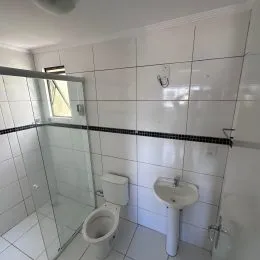Banheiro com revestimento de azulejos brancos e louças sanitárias.