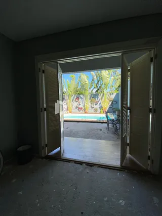 Interior de uma sala com porta de vidro abrindo para um pátio externo com vegetação.