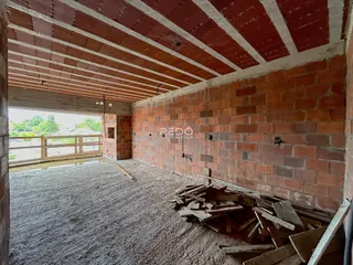 Interior de uma área em construção com paredes de tijolo aparente e teto de vigas.