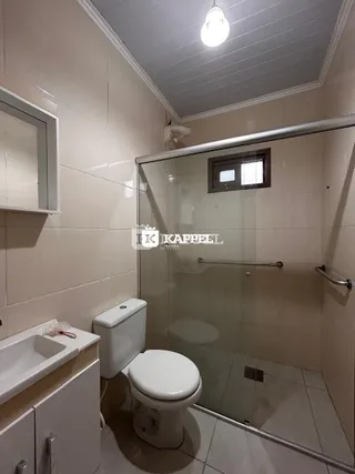 Foto interna de um banheiro com box de vidro e vaso sanitário.