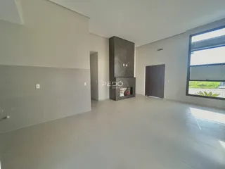 Interior de uma sala ampla com paredes brancas e lareira de mármore.