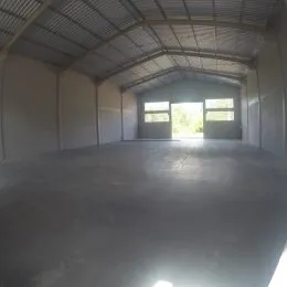 Vista interna de um espaço amplo com teto metálico e piso de concreto.