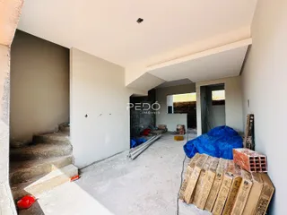 Vista interna de um corredor em construção com paredes brancas e piso de concreto.