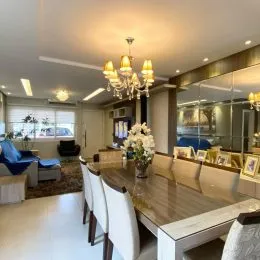 Imagem de uma sala de estar com mesa de madeira e iluminação clara.