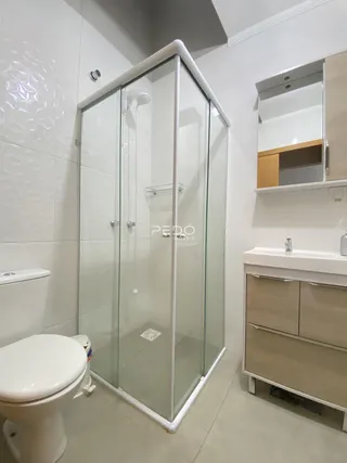 Banheiro com box de vidro e louças brancas em um imóvel.