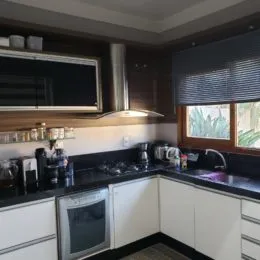 Cozinha com armários escuros e televisão montada na parede.