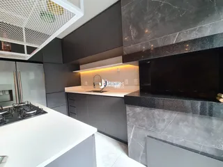Interior de uma cozinha moderna com armários escuros e bancadas claras.