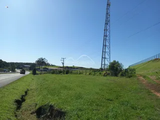 Vista de um campo gramado ao lado de uma estrada com uma torre de energia ao fundo.
