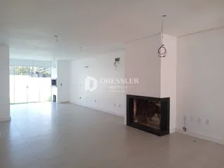 Ambiente interno de uma sala ampla com parede branca e lareira em uma residência.