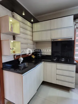 Vista interna de uma cozinha com armários brancos e bancada escura.