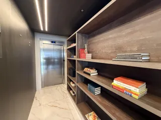 Hall de entrada com prateleiras de madeira e piso de mármore claro.