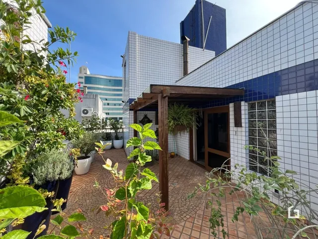 Vista externa de um pátio com piso de tijolos e vegetação.