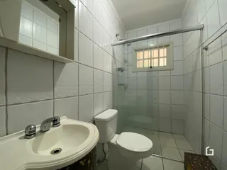 Banheiro com revestimento cerâmico branco e box de vidro.