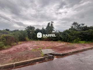 Vista externa de um terreno com vegetação densa e área de terra vermelha.