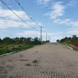 Vista de uma estrada pavimentada com vegetação ao fundo sob um céu parcialmente nublado.