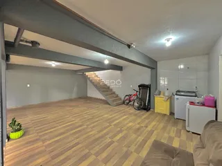 Interior de uma sala de estar com piso de madeira e escadaria visível.