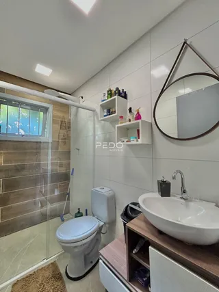 Banheiro com revestimento cerâmico e box de vidro transparente.