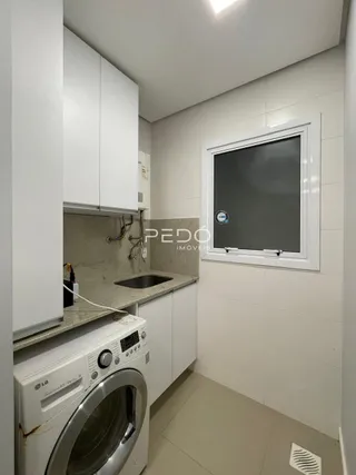 Vista interna de uma área de serviço com máquina de lavar roupa e armários brancos.