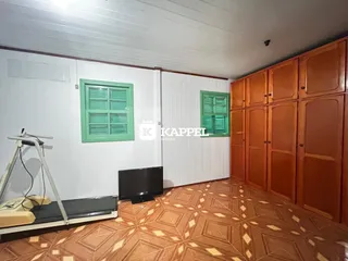 Uma sala de estar com paredes brancas, piso de madeira e janelas com venezianas verdes.