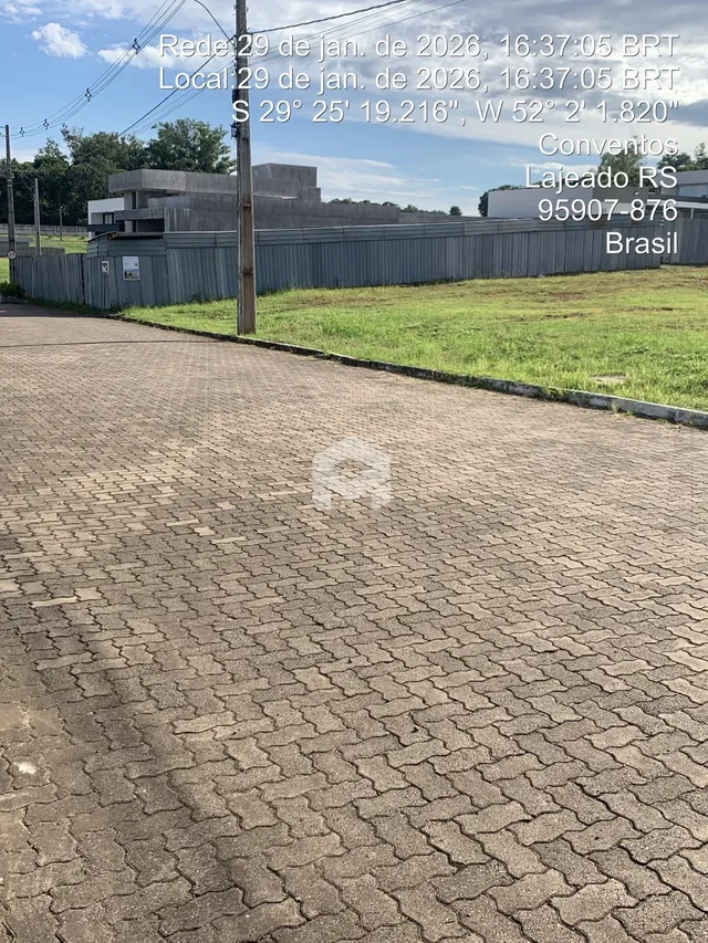 Vista externa do terreno com cerca de madeira e pavimento de tijolos.