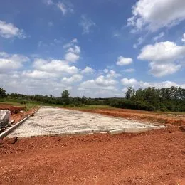 Área externa de terra vermelha com vegetação rasteira sob um céu azul.