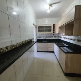 Foto interna de uma cozinha com armários brancos e bancadas escuras.