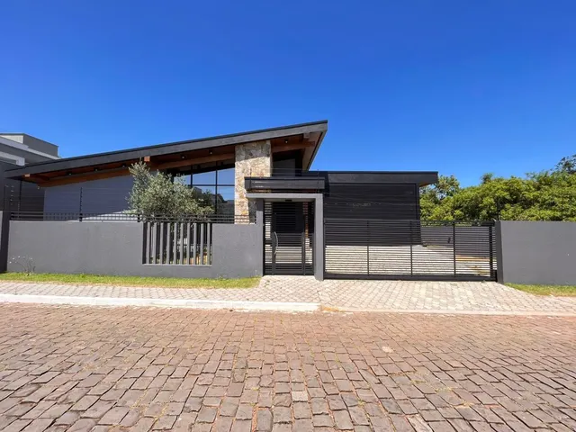 Fachada externa de uma casa moderna com revestimento escuro e piso de tijolos na rua.
