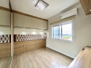 Quarto com cabeceira estofada e piso de madeira clara.