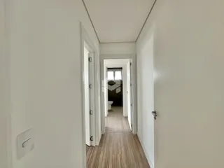 Corredor interno de uma residência com piso de madeira clara.