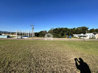 Vista externa de um terreno com grama seca e estruturas ao fundo.