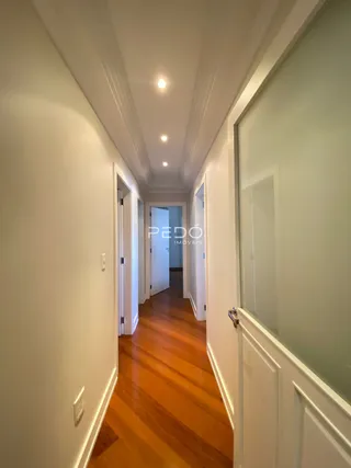 Corredor interno de uma residência com piso de madeira e paredes brancas.