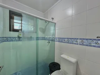 Foto de um banheiro com box de vidro e azulejos brancos.