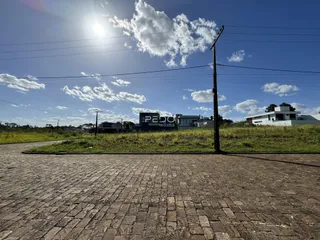 Vista externa de uma propriedade com pavimento de paralelepípedos e vegetação ao fundo.