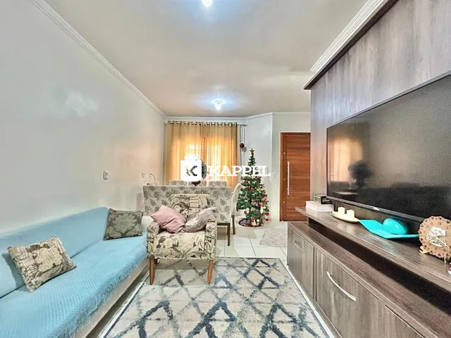 Sala de estar com sofá azul e poltronas decorativas e televisão na parede.