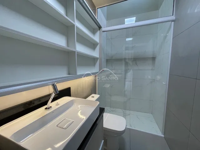 Banheiro com bancada branca e box de vidro transparente.