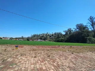 Vista de uma propriedade rural com campos verdes e vegetação ao fundo.