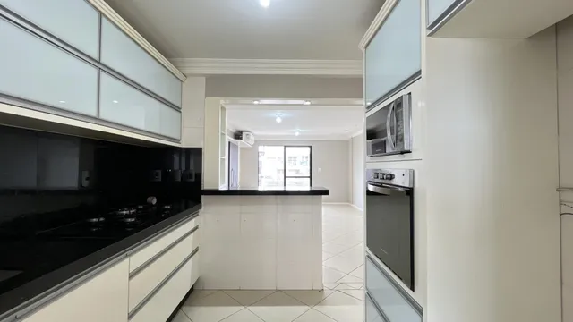 Vista interna de uma cozinha moderna com armários brancos e bancadas escuras.