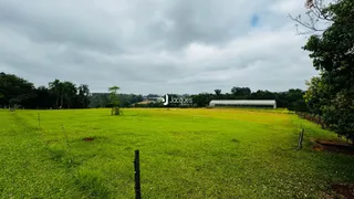 Campo verde aberto com vegetação e uma estrutura ao fundo.