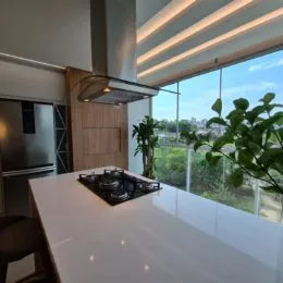 Vista de uma cozinha moderna com bancada branca e fogão preto.