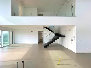 Ambiente interno de um apartamento moderno com pé direito alto e escadaria.