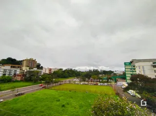 Vista externa de uma área gramada com árvores e uma estrada.