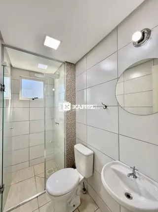 Foto interna de um banheiro com revestimento de azulejos brancos e box de vidro.