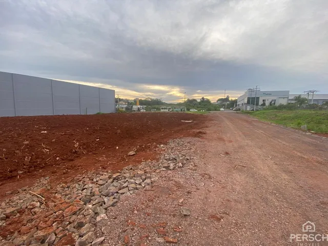 Vista externa de um terreno com solo avermelhado e uma estrada de terra sob um céu nublado.
