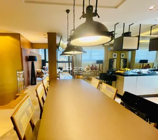 Vista de uma sala de jantar com iluminação pendente e área de cozinha em um imóvel.