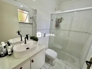 Banheiro com pia branca, box de vidro e revestimento cerâmico.