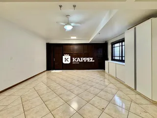 Sala ampla com piso de cerâmica clara e painéis de madeira no fundo.