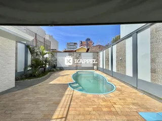 Piscina externa com deck de tijolos em uma área de lazer residencial.