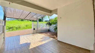 Área externa pavimentada com vista para um campo verde.