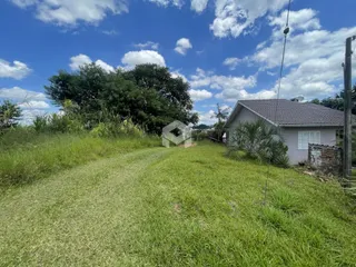Vista externa de uma residência com gramado verde e vegetação ao fundo.