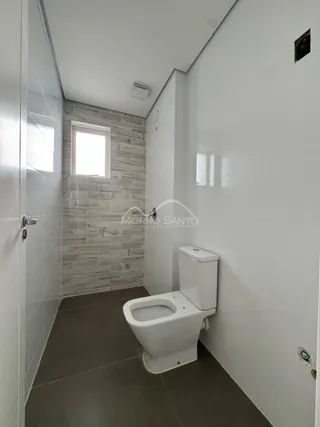 Foto de um banheiro com revestimento de pedra clara e piso escuro.
